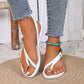 White Rhyzak women's bohemian flat sandals with toe loop and adjustable ankle strap, shown on model's feet wearing denim jeans on a woven mat.