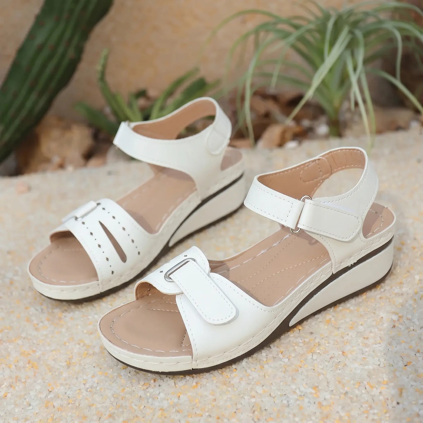 White Lyraia women's low wedge sandals with peep-toe, perforated front straps, and adjustable hook-and-loop closures, set against a sandy background.