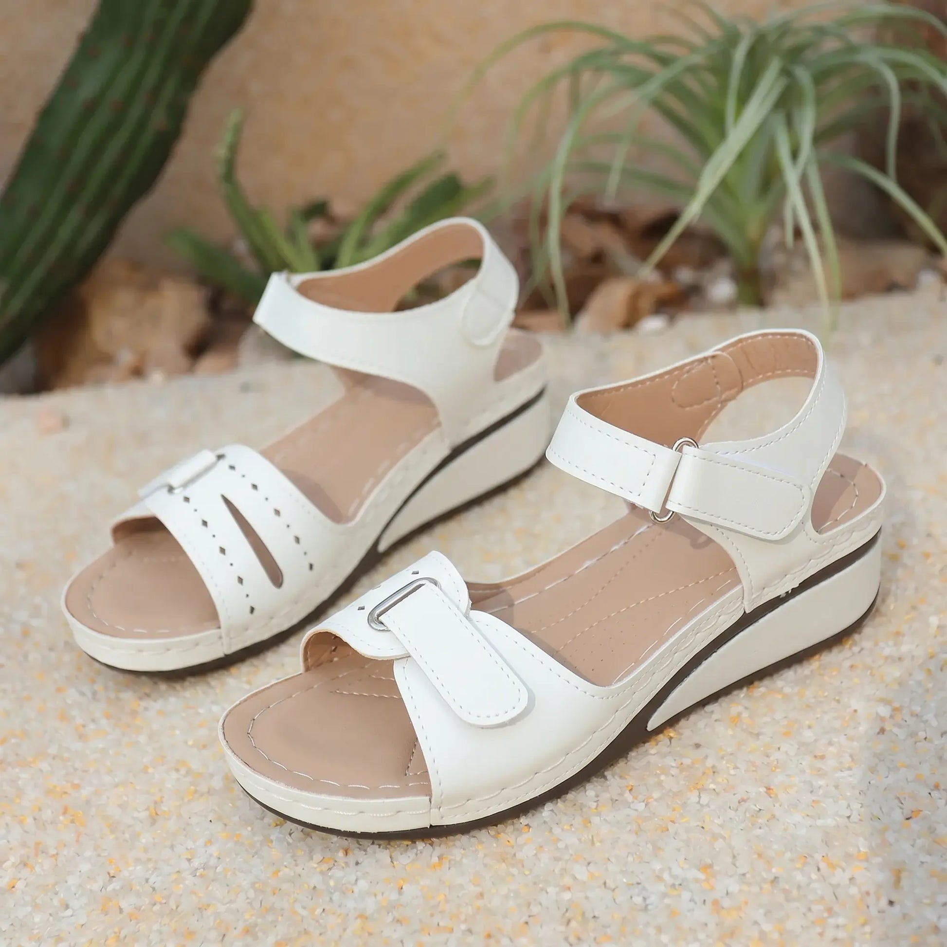 White Lyraia women's low wedge sandals with peep-toe, perforated front straps, and adjustable hook-and-loop closures, set against a sandy background.