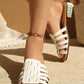 Elegant white woven flat slide sandals worn by a woman with an embellished block heel, showcasing artisanal strap detail and a chic peep-toe silhouette in a sunlit, bohemian setting.