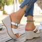 Model wearing white woven platform espadrille sandals with T-strap and buckle detail, paired with distressed denim jeans and a turquoise anklet, set against an outdoor wooden deck backdrop.