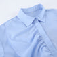 Close-up of a women's powder blue collared blouse featuring asymmetrical ruffle detailing down the front placket and a discreet size tag on the collar.