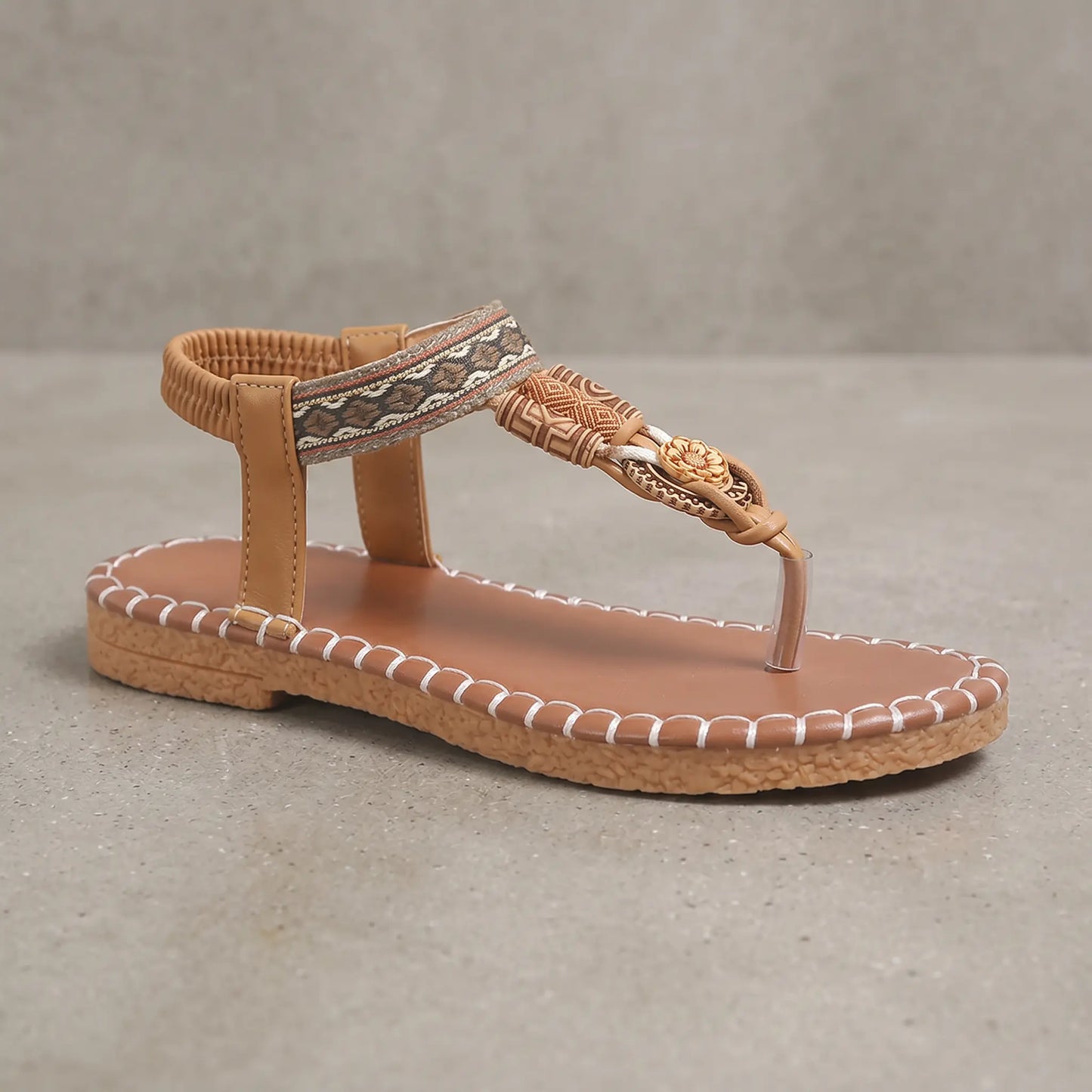 Bohemian flat thong sandal in Rich Earth Brown, featuring a woven patterned strap, floral beaded embellishment, and a distinctive stitched-effect sole.