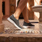 Zhivra women's grey knit slip-on comfort sneakers, featuring breathable mesh and thick white soles, worn by a woman walking on ornate patterned tiles.