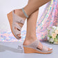 Women's Khaki perforated leather peep-toe wedge sandals with an adjustable hook-and-loop strap, detailed with white contrast stitching and a wood-effect wedge heel, shown on a model's feet with a sparkling anklet.