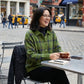 A woman wearing a green and navy women's soft knit plaid shirt with a relaxed fit, sitting at an outdoor cafe table with a coffee.