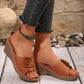Women's tan wedge sandals with a large floral rose embellishment and white contrast stitching, styled with distressed jeans and an anklet.