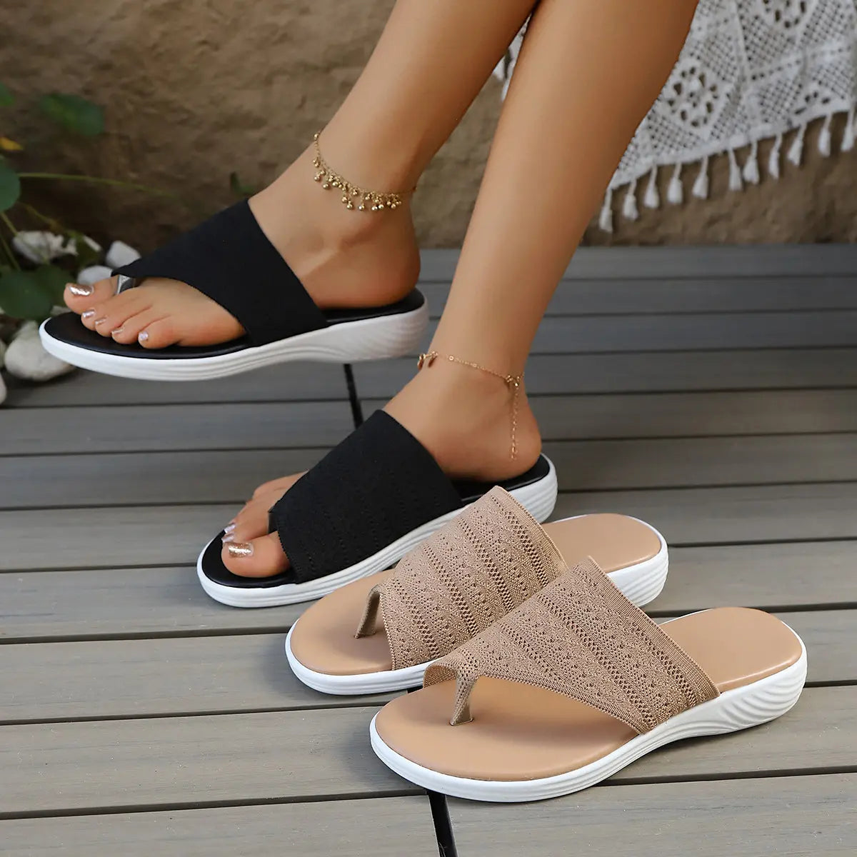 Beige and black woven comfort slides with geometric diamond knit straps are showcased on a model's feet resting on a wooden deck.