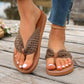 Close-up of feet wearing brown bohemian woven strap flat thong sandals with a tan sole, styled on a wooden deck.