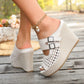 Cream woven wedge sandals with peep toe and dual buckle straps worn by a woman, showcasing the artisanal raffia texture and comfortable wedge heel on a wooden deck.