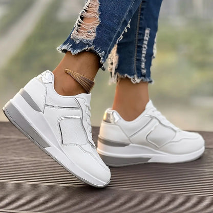 Women's white Xanthe wedge sneakers with rose gold accents, worn with ripped blue jeans, featuring a textured panel and a layered grey/white sole from a three-quarter side view.