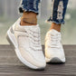 Women's off-white low-top sneakers with textured panels and subtle rose gold metallic accents, worn with ripped denim jeans and a gold anklet on a wooden surface.