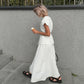 Elegant white V-neck sleeveless top paired with a flowing A-line midi skirt, worn by a woman walking outdoors with an ice cream cone. The sophisticated two-piece set showcases a timeless design with a matte finish.