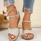 Elegant pale gold peep-toe wedge sandals with delicate sequined embroidery and a polished gold trim, styled on a woman's feet with distressed denim jeans. Features an adjustable ankle strap for a secure fit.