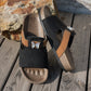 Xylia women's embellished slide sandals in Onyx Black featuring a contoured cork footbed, tan accent strap, and a clear crystal butterfly embellishment. Shown from a three-quarter angle on a wooden deck.