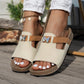 Women's Xylia embellished slide sandals in cream with a tan accent strap and sparkling butterfly detail, worn on feet with white pedicure. Features a cork footbed and flat natural rubber sole, styled on a wooden deck.