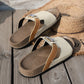 Xylia embellished flat slide sandals in cream and tan, featuring a clear crystal butterfly accent and a cork footbed, styled on a straw hat and wooden deck.
