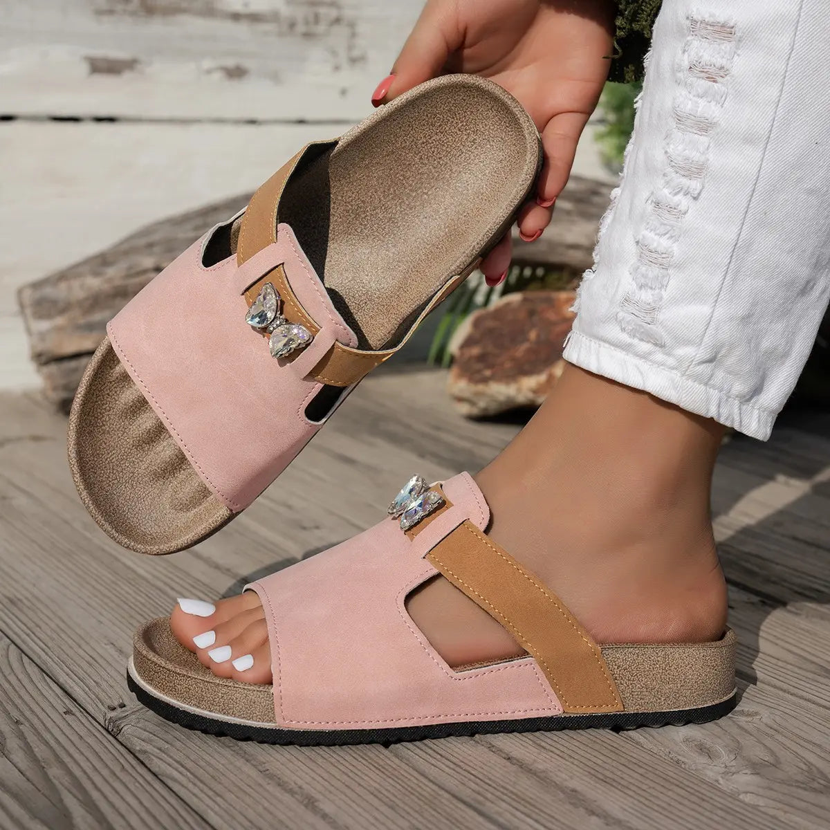 Xylia blush pink embellished flat slide sandals shown on a model's foot, featuring a sparkling butterfly detail and comfortable cork footbed.