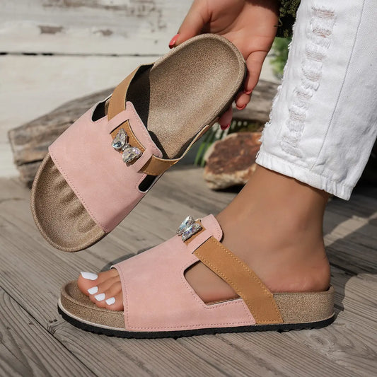 Xylia blush pink embellished flat slide sandals shown on a model's foot, featuring a sparkling butterfly detail and comfortable cork footbed.