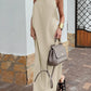 A woman models the Xylos Halter Neck Maxi Dress in light beige cotton-linen blend, featuring a flowing A-line silhouette and a tie-back halter neckline, outdoors on a brick pathway.