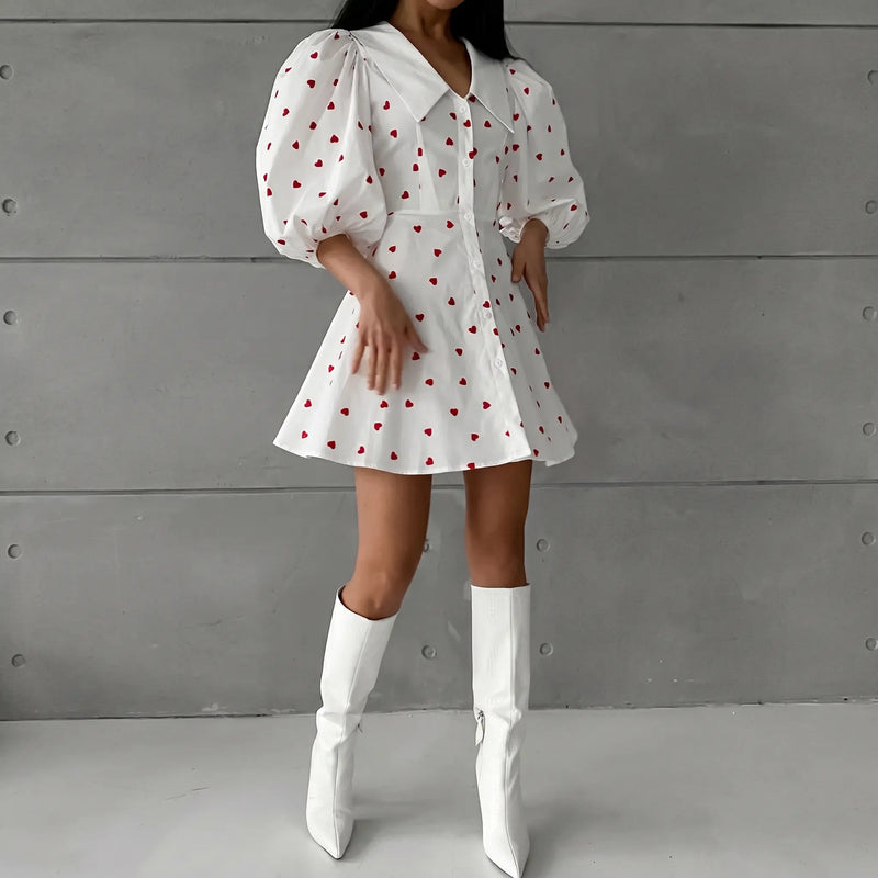 Xylos heart print puff sleeve dress, featuring a crisp pointed collar, A-line silhouette, and button-down front, showcased on a model in white boots against a grey textured studio backdrop.