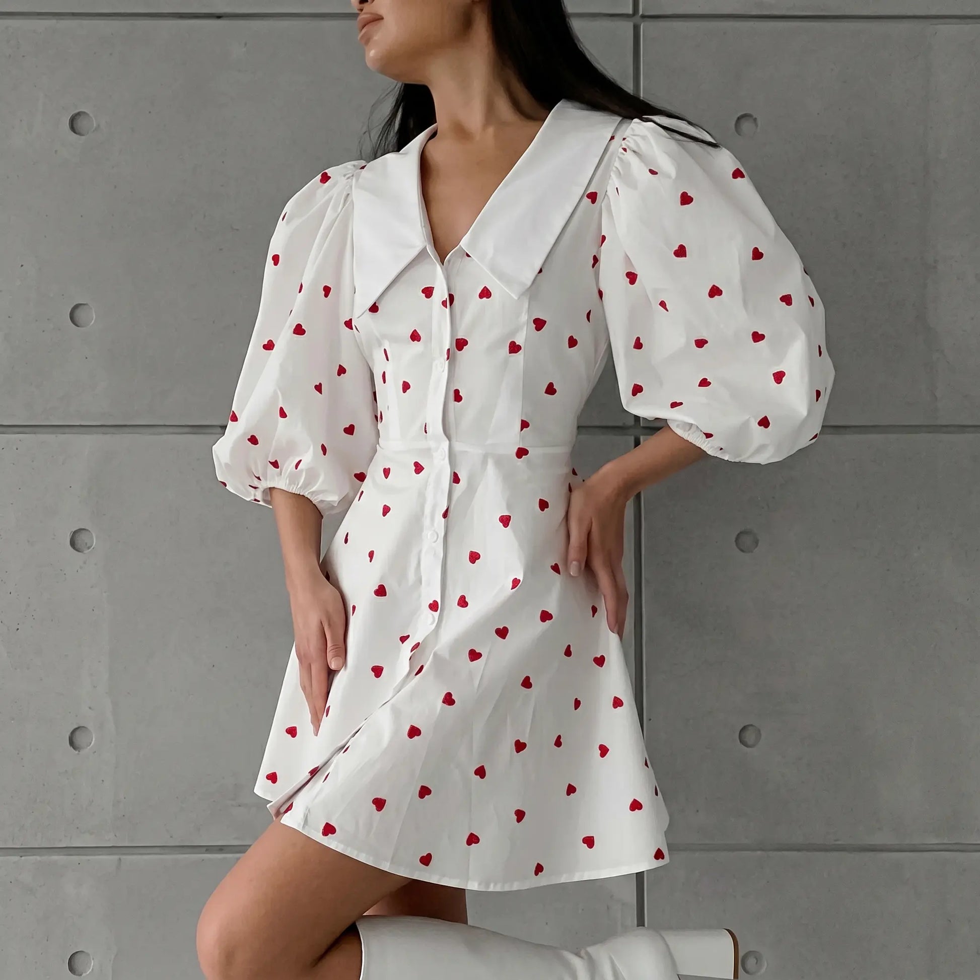 A woman wearing a white Xylos heart print puff sleeve dress with a pointed collar and A-line skirt, shown in a front three-quarter view against a textured grey studio background.