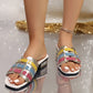 Xylos women's multi-color woven block heel slides featuring metallic gold, pink, blue, and yellow straps, a square toe, and a glitter block heel, styled on feet with white toenails and an anklet on a reflective surface.
