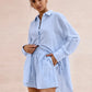 Woman modeling a Xylos textured cotton set in pale sky blue, featuring an oversized camp collar shirt and relaxed-fit shorts, against a blush pink background.