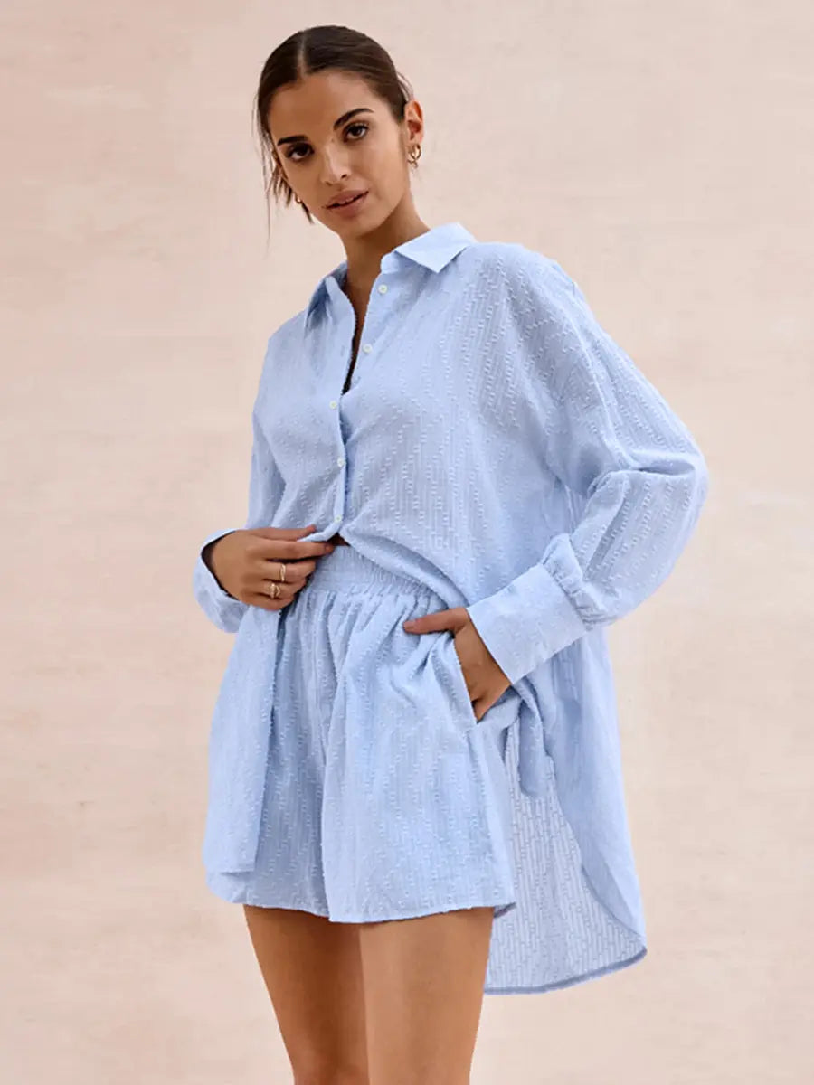 Woman modeling a Xylos textured cotton set in pale sky blue, featuring an oversized camp collar shirt and relaxed-fit shorts, against a blush pink background.