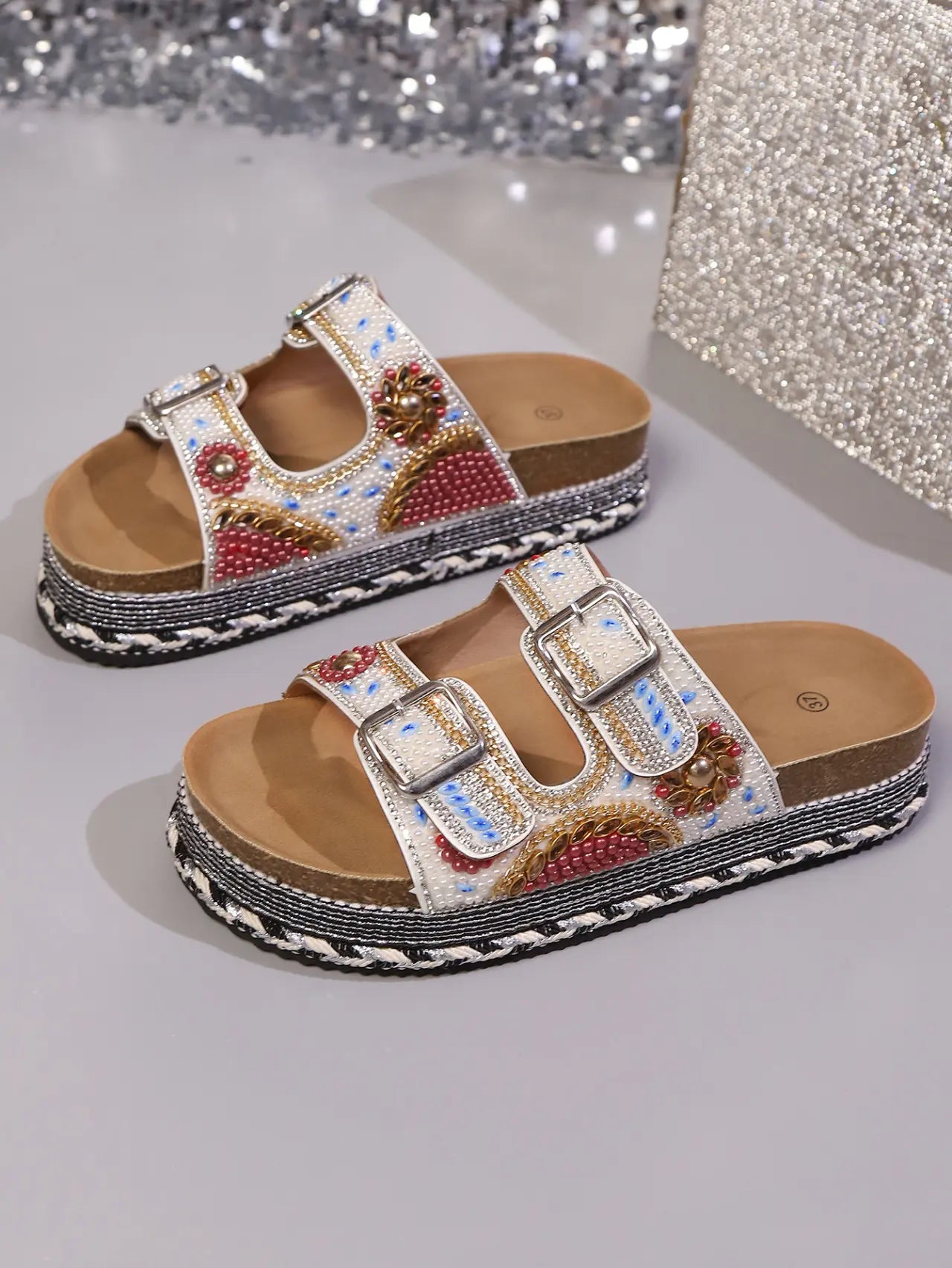 Xylos embellished platform slide sandals in white fabric with vibrant bead and sequin floral patterns, featuring double adjustable buckle straps and a cork-effect layered sole.