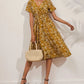 Woman wearing a yellow ditsy floral print midi dress with short flutter sleeves and a V-neckline, paired with black heels and a straw bag.