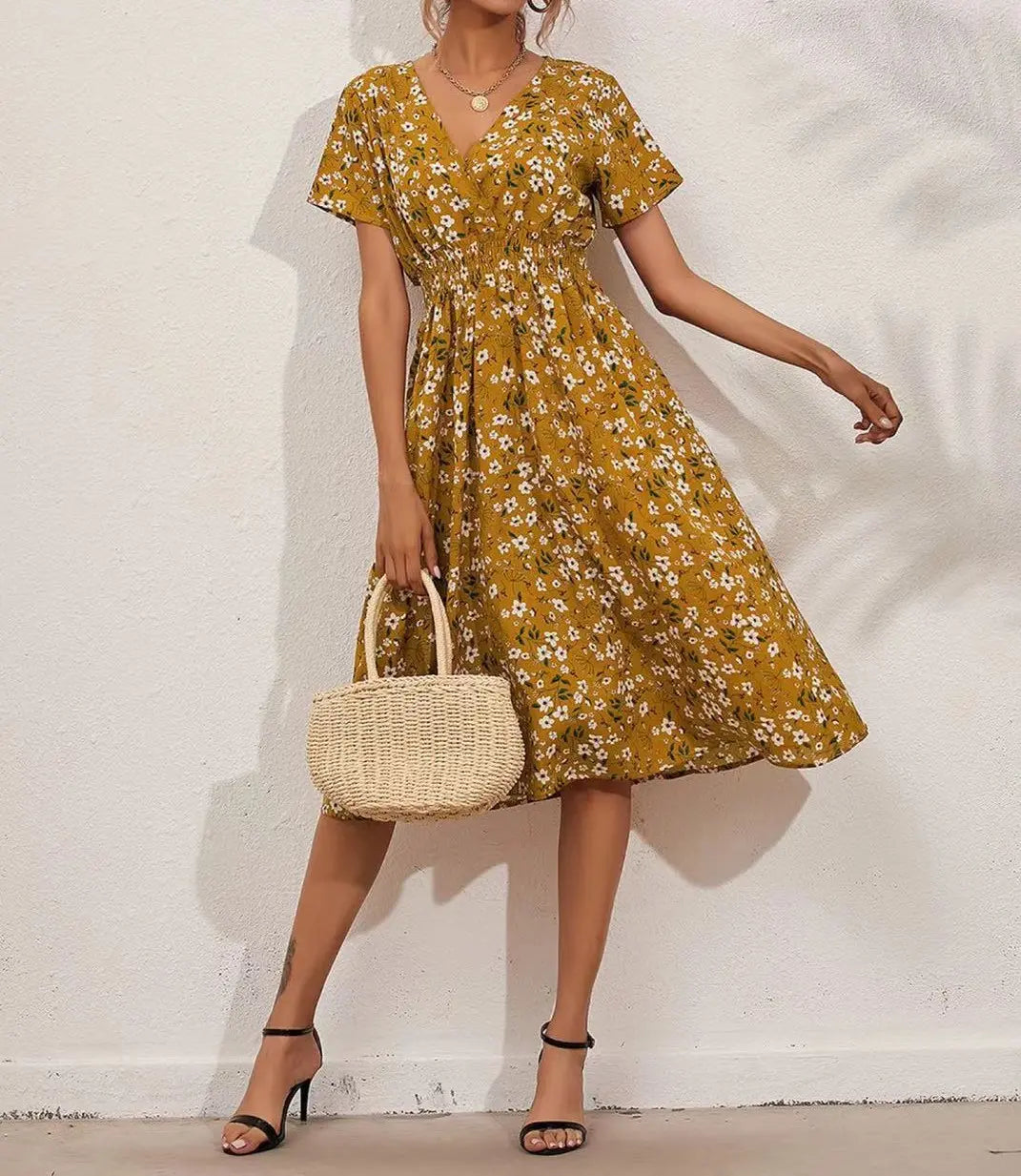 Woman wearing a yellow ditsy floral print midi dress with short flutter sleeves and a V-neckline, paired with black heels and a straw bag.
