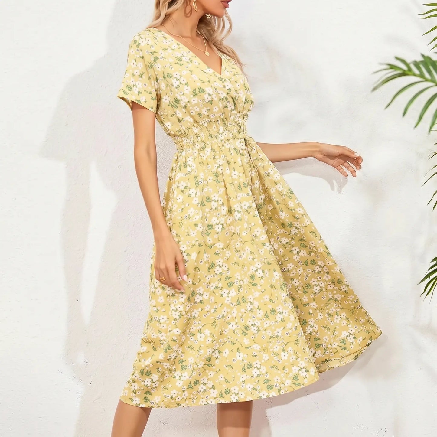 A woman models a yellow ditsy floral midi dress with a V-neck, short flutter sleeves, and a cinched smocked waist, styled for a summer day.
