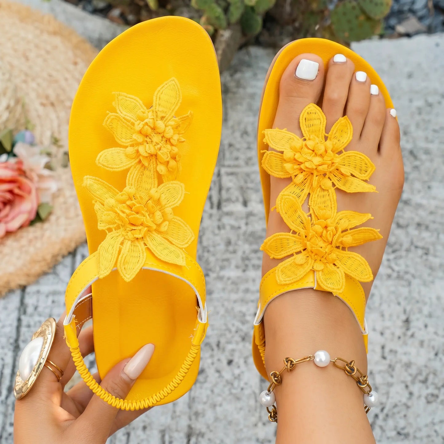 Sunny yellow flat summer sandals for women, featuring delicate layered fabric floral appliqués and a comfortable elasticated slingback strap, worn on feet in a casual outdoor setting.