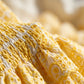 Close-up of the Radiant Yellow Taziro mini dress, showcasing the intricate smocked bodice detail transitioning to the delicate eyelet-embroidered tiered ruffle skirt with scalloped edges.
