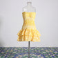 Yellow strapless mini dress with smocked bodice, tiered eyelet-embroidered ruffle skirt, and scalloped edges, front view on mannequin.