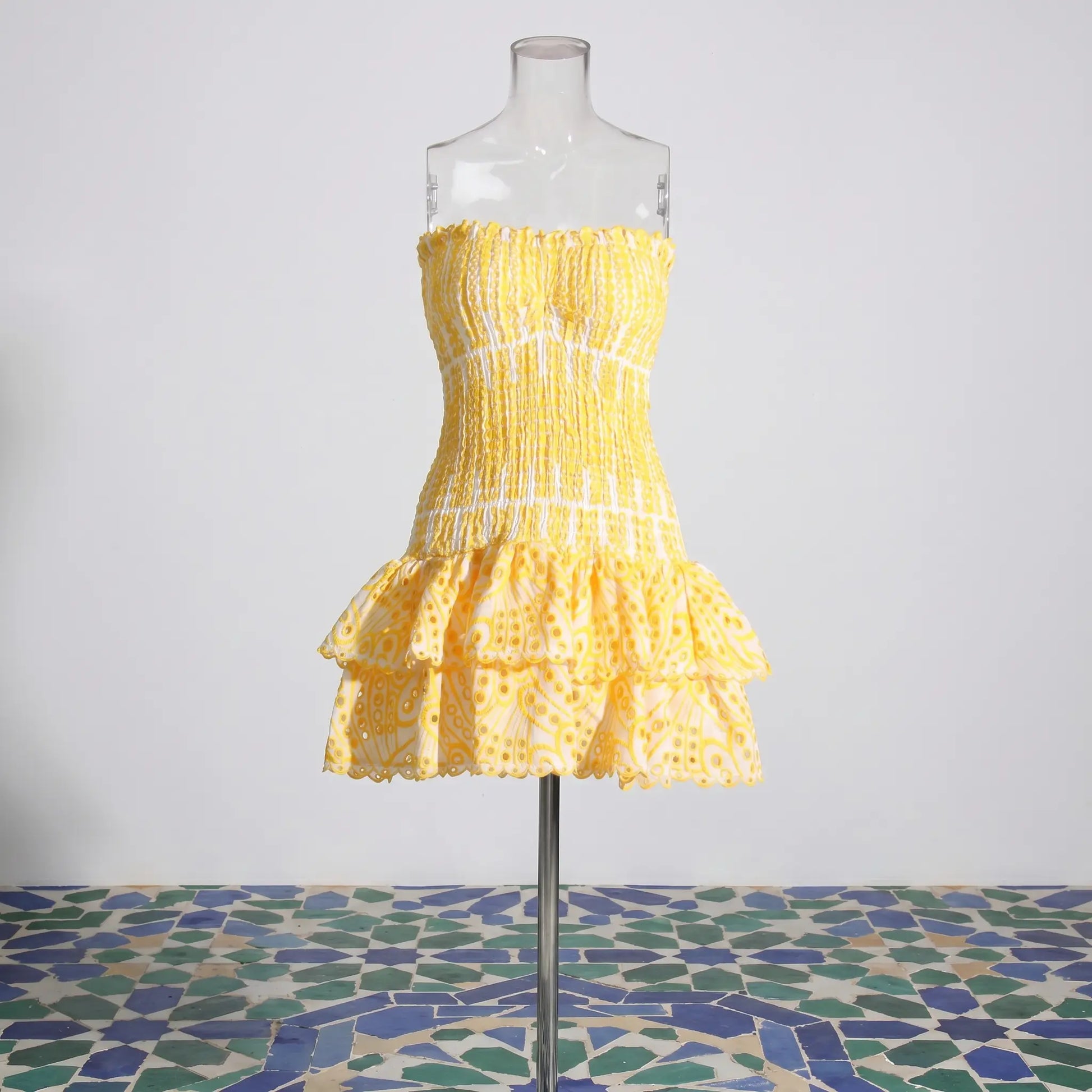 Yellow strapless mini dress with smocked bodice, tiered eyelet-embroidered ruffle skirt, and scalloped edges, front view on mannequin.