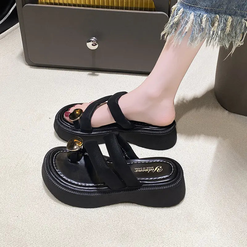 Black Zalva platform thong sandals with plush velvet-feel straps and a polished gold-tone circular buckle, shown on a foot with a layered sole.
