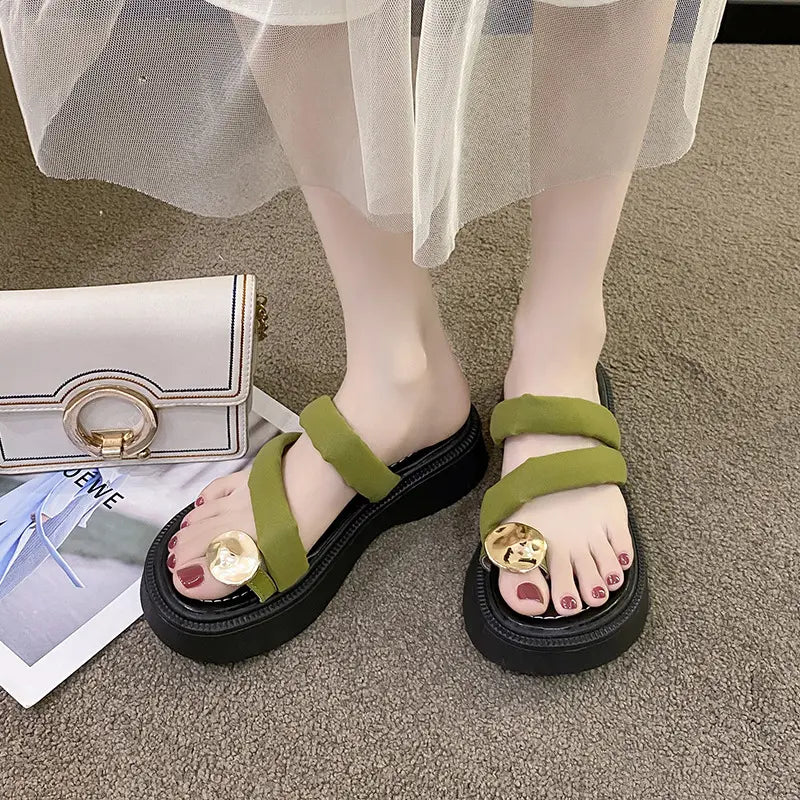 Olive green Zalva platform thong sandals worn on feet, featuring plush straps and a gold circular buckle, styled with a white handbag and magazine.