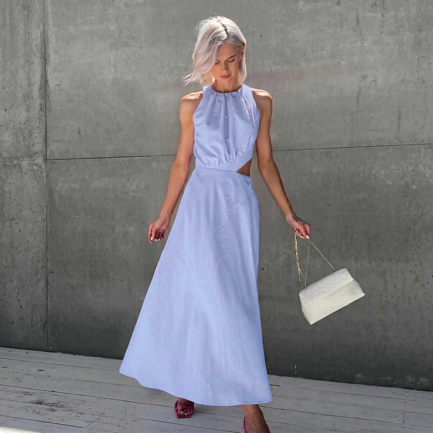 A romantic Zarion sleeveless midi dress in Periwinkle Sky, featuring a gathered halter neckline and dramatic side waist cut-outs, shown on a model against a grey wall.