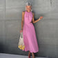 Model wearing a pink sleeveless gathered halter neck midi dress with elegant side waist cut-outs, holding a mesh bag of lemons.