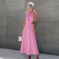 A woman models a sleeveless Zarion pink midi dress with romantic gathered halter neckline and dramatic side waist cut-outs, set against a textured grey wall.