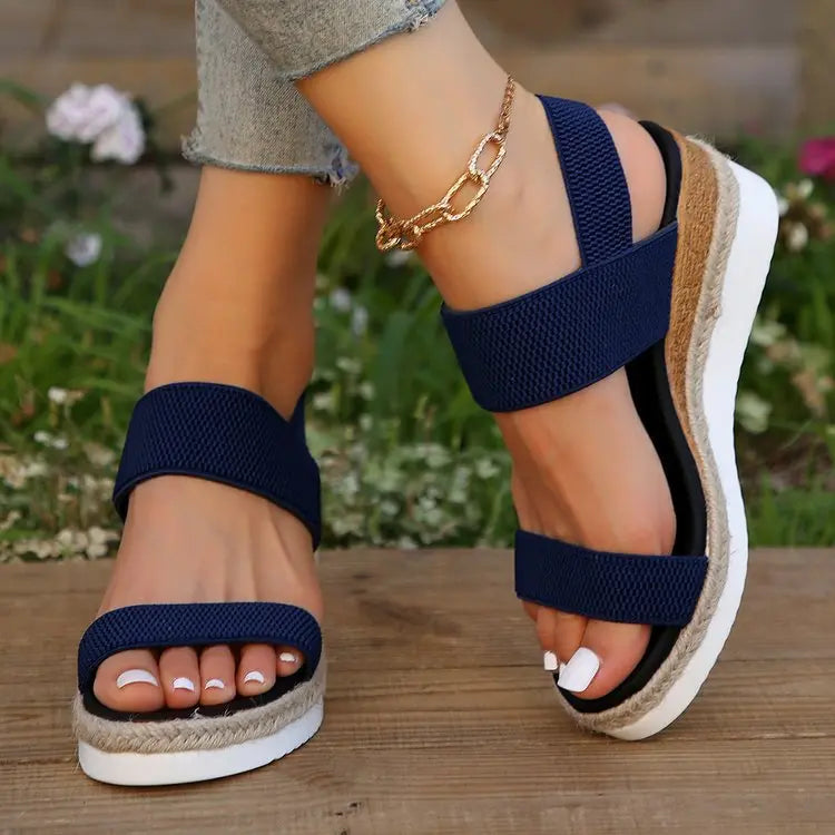 Zaylin navy blue espadrille wedge sandals worn on feet with a gold-tone ankle chain, showcasing elasticated straps and a peep-toe design against a natural outdoor backdrop.