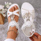 Elegant white Zaylor flat sandals adorned with delicate floral lace, pearls, and a shimmering rhinestone buckle, shown on a foot with a gold anklet.