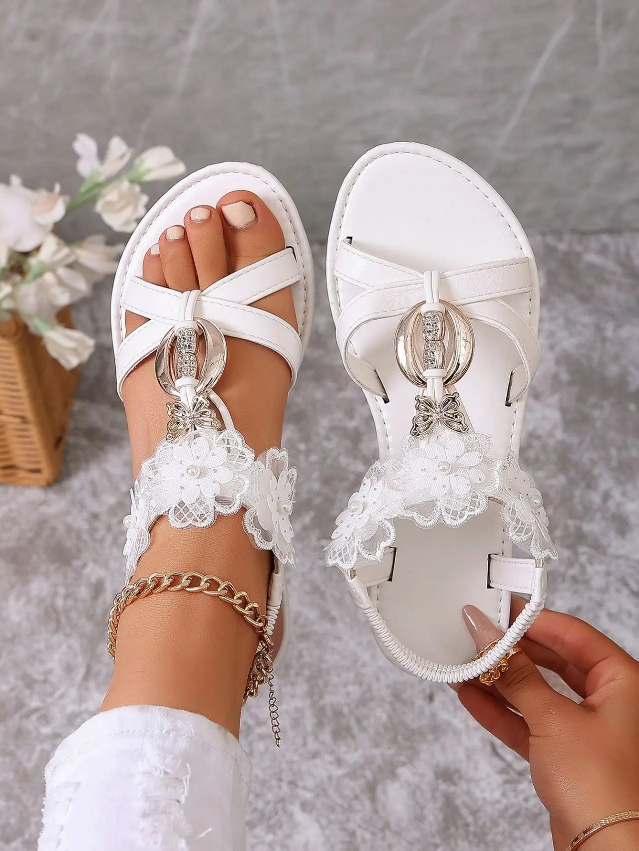 Elegant white Zaylor flat sandals adorned with delicate floral lace, pearls, and a shimmering rhinestone buckle, shown on a foot with a gold anklet.