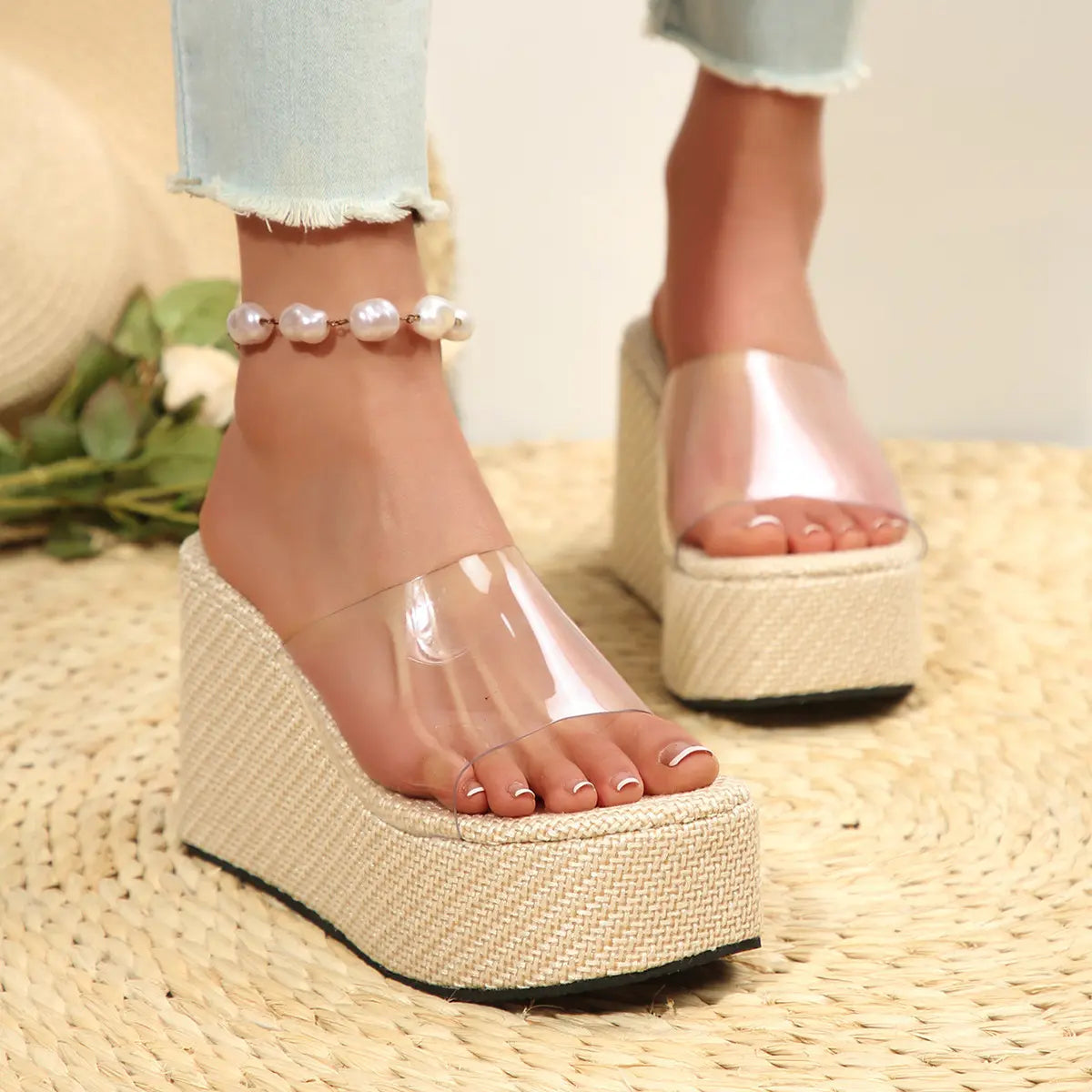 Women's Zelka clear strap wedge slide sandals in almond beige, worn with distressed jeans and a pearl anklet on a woven mat.