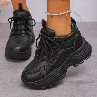 Black Zelpha chunky platform sneakers worn on feet with embellished grey denim jeans and a pearl anklet, showcasing the smooth synthetic leather upper and lugged rubber sole.
