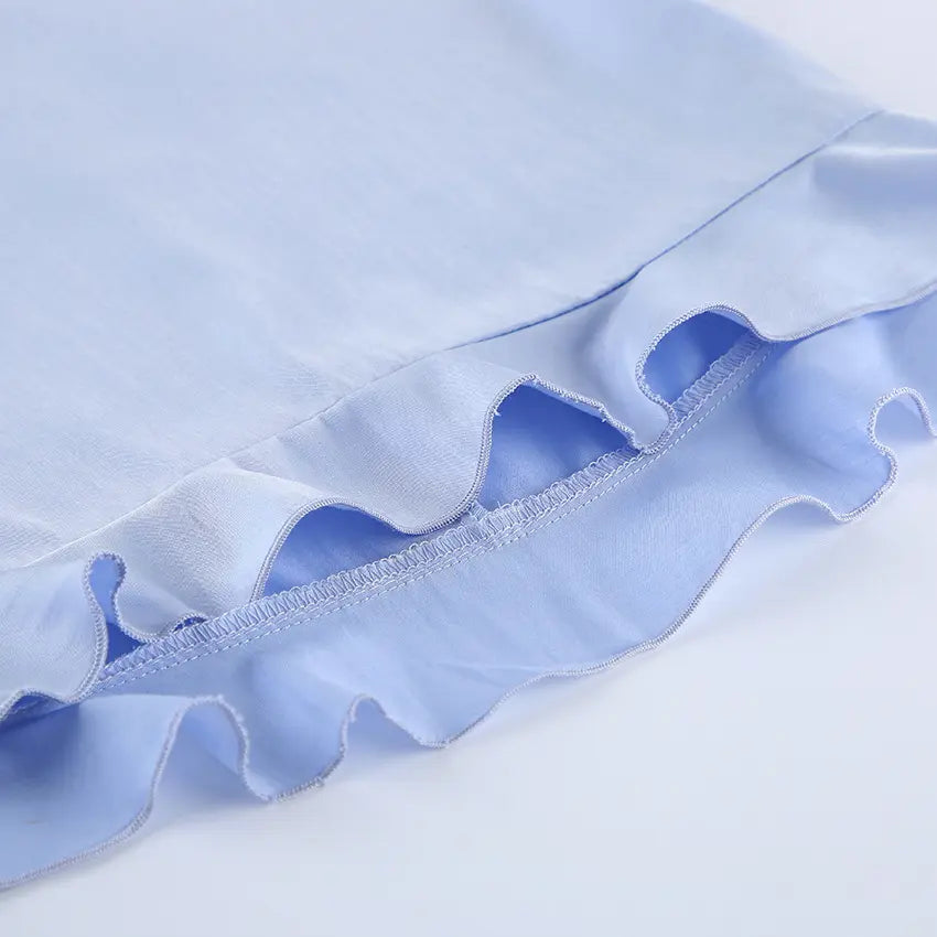 Close-up view of light blue Zelphira bohemian set fabric showing a delicate ruffled hem and visible stitching, highlighting the fluid drape and premium material blend.