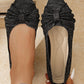 Zendari elegant black knit pointed-toe flats with a decorative bow accent, shown on a foot and held by a hand against a textured background.