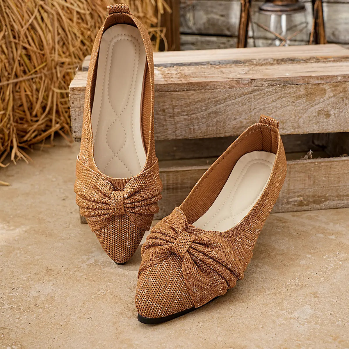 Zendari elegant pointed-toe knit flats in bronze with a shimmering metallic thread and a delicate bow accent, shown from three-quarter and side views on a textured surface with rustic background elements.